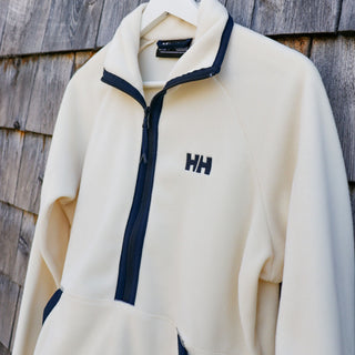 Beige fleece jacket with navy zipper and Helly Hansen logo on a wooden background